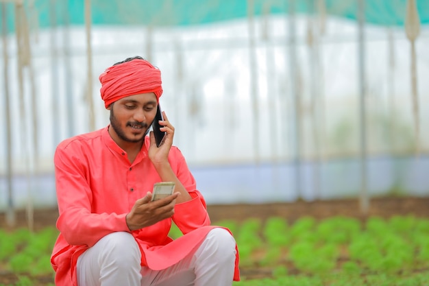 Young indian farmer using smartphone at greenhouse