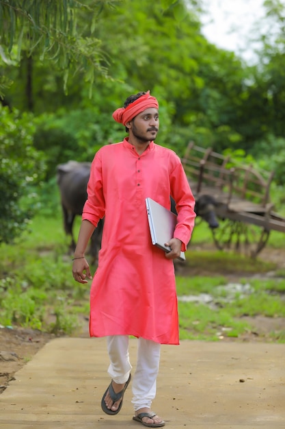 Young indian farmer with laptop at field