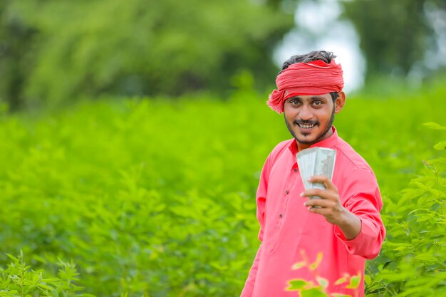 Young indian farmer with money on the field