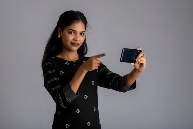 Young Indian girl using a mobile phone or smartphone on gray