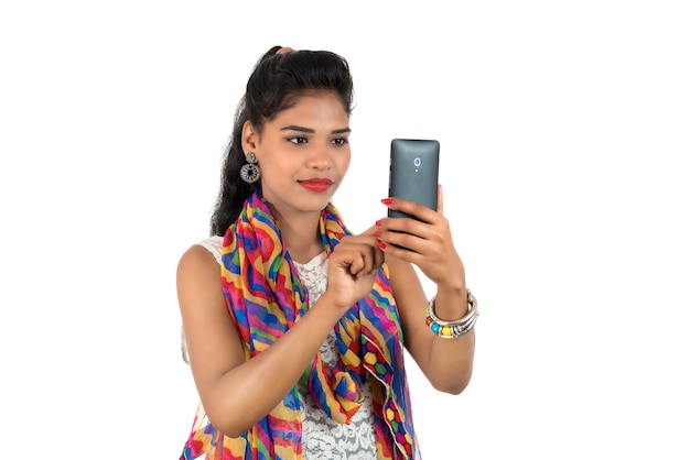 Молодая индийская девушка с помощью мобильного телефона или смартфона, изолированные на белом фоне