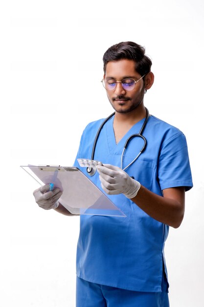 Young indian male doctor dressed in uniform with stethoscope taking notes in notepad isolated over white background.