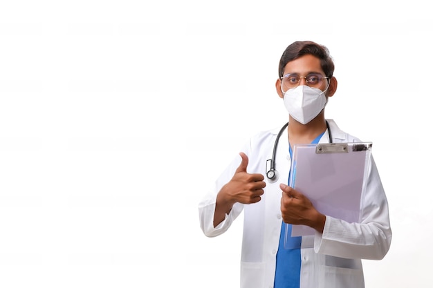 Молодой индийский мужчина-врач, одетый в униформу со стетоскопом, делая заметки в блокноте, изолированном на белом фоне.