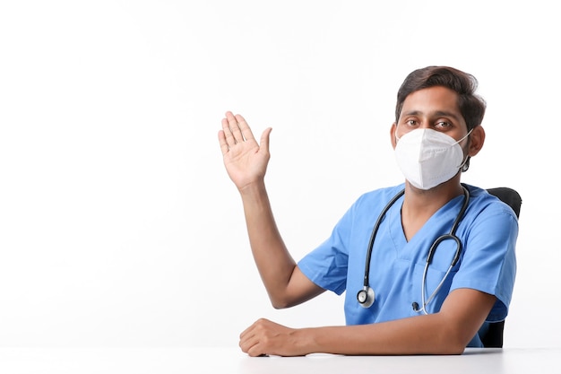 Young indian male doctor wearing mask and pointing with hand at clinic.