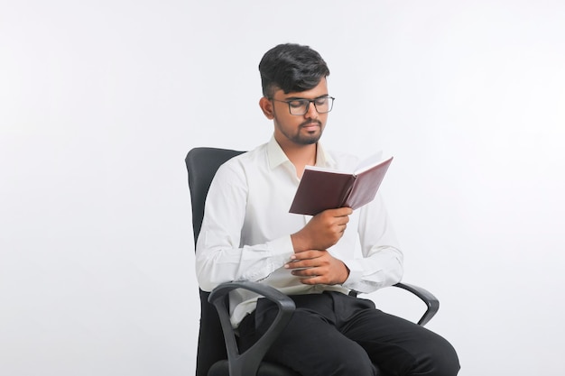 白い背景の上の日記を読んで若いインド人男性。