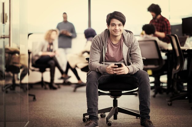 young indian male software developer using mobile phone writing messages while having break at modern creative startup office