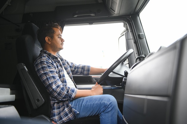 若いインド人の男性トラック運転手が車輪の後ろに座っている