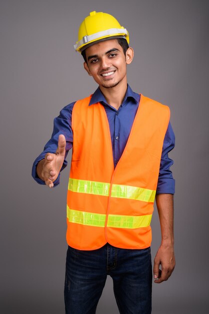 Young Indian man construction worker against gray wall