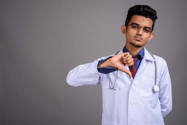 Young Indian man doctor against gray wall