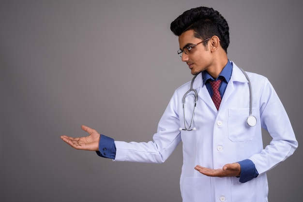 Young Indian man doctor against gray wall