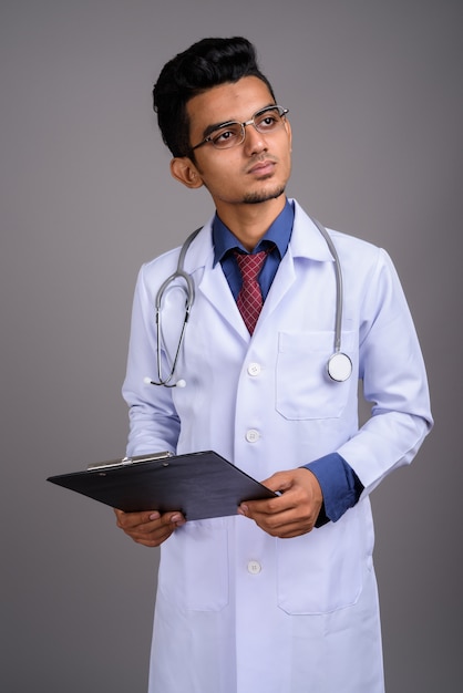 Young Indian man doctor against gray wall