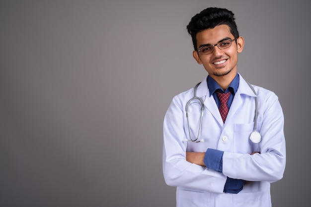 Young Indian man doctor against gray wall