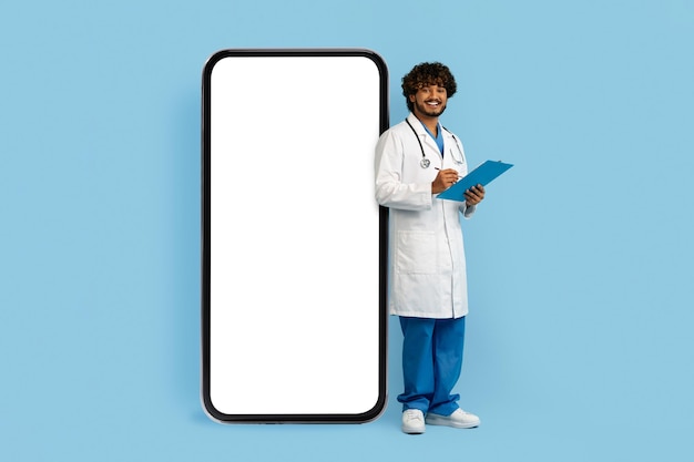 Young indian man doctor standing by huge phone