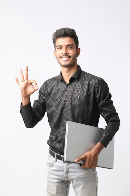 Молодой индийский мужчина держит ноутбук в руке на белом фоне.