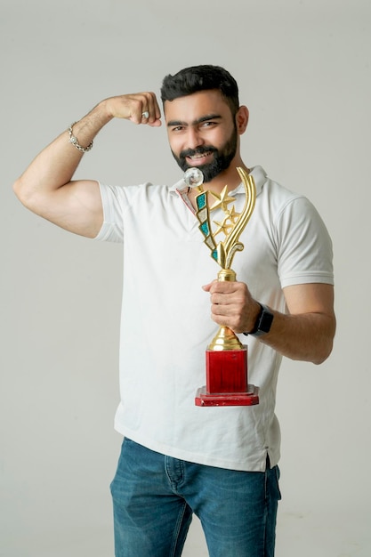 Photo young indian man holding a trophy and doing winner gesture