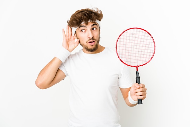 Young indian man playing badminton trying to listening a gossip.