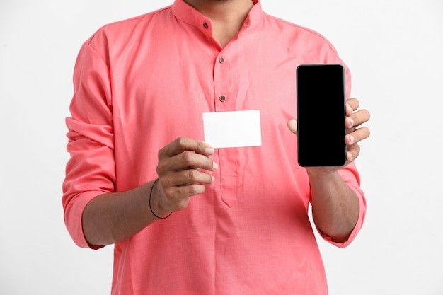 Young indian man showing card and smartphone on white wall