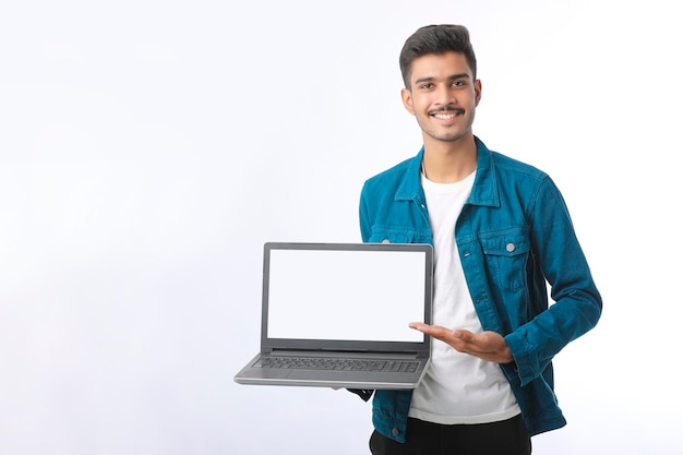 Giovane indiano che mostra lo schermo del computer portatile su sfondo bianco.