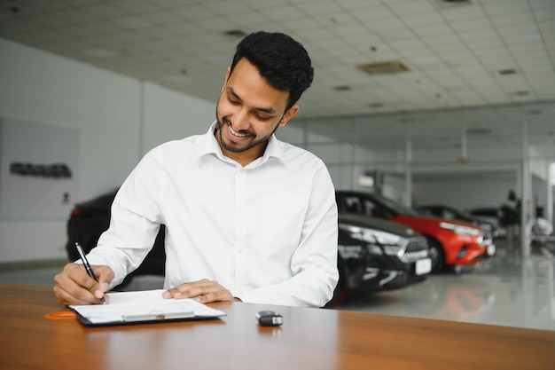 Young indian man signing documents at car dealership