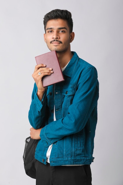 Young Indian man standing and holding dairy in hand on white background.