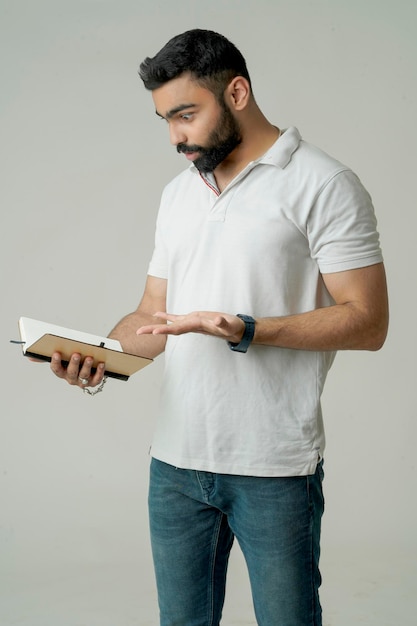 白に隔離されたノートブックで立っている若いインド人男性