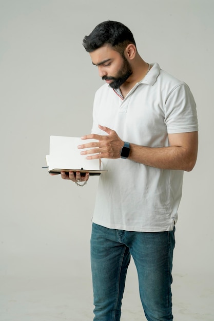 白に隔離されたノートブックで立っている若いインド人男性