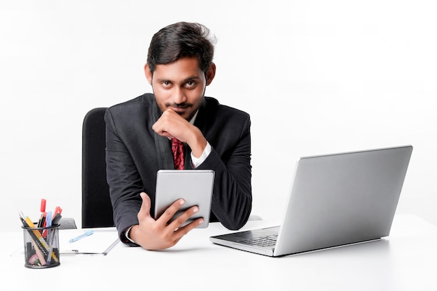 Молодой индийский мужчина в костюме и с помощью планшета и ноутбука в офисе
