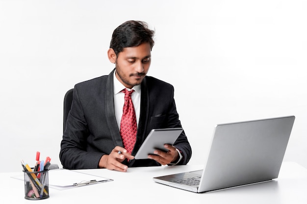 Young indian man in suit and using tablet and laptop at office