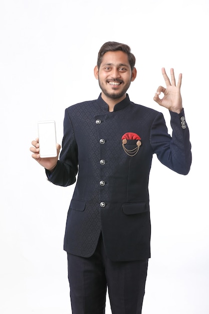 Young indian man in tradition wear and showing smartphone screen on white background.