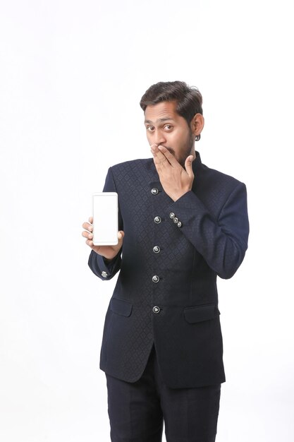 Young indian man in tradition wear and showing smartphone screen on white background.