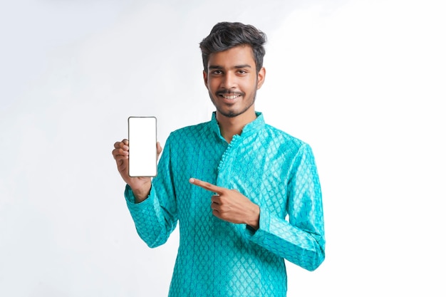 Young indian man in tradition wear and showing smartphone screen on white background.