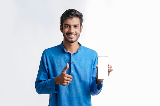 Young indian man in tradition wear and showing smartphone screen on white background.