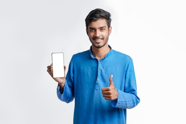 Young indian man in tradition wear and showing smartphone screen on white background.