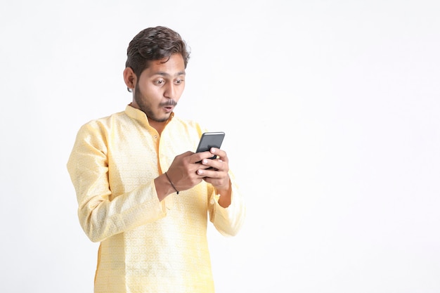 Young indian man in tradition wear and using smartphone on white wall