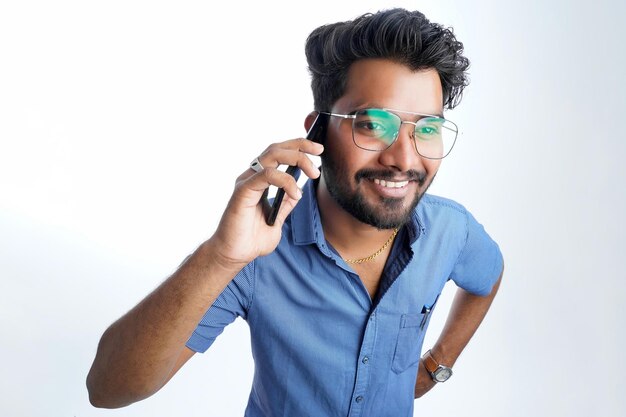 Young indian man using smart phone standing over isolated white\
background serious face thinking about question or solution very\
confused idea