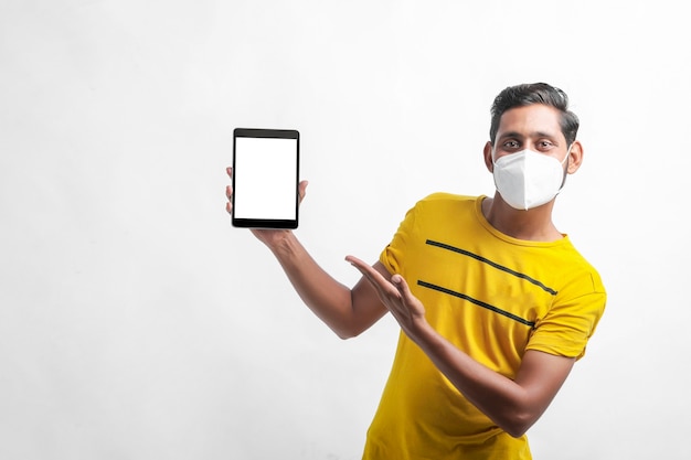 Young indian man wearing mask and showing tablet