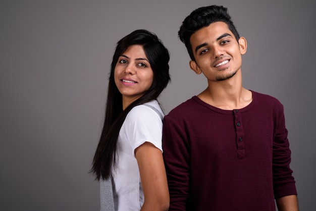 Young Indian man and young Indian woman together on gray wall