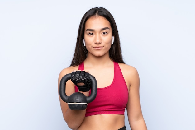 Young Indian sport woman on blue wall making weightlifting with kettlebell