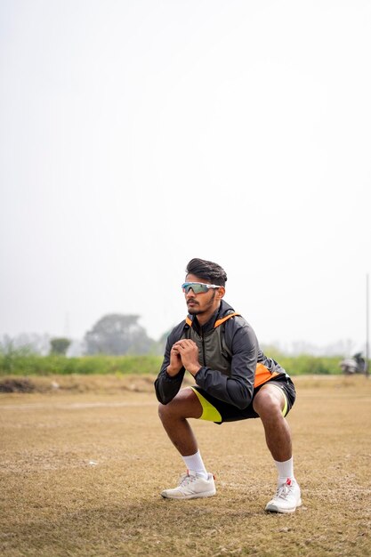 Young indian sports man doing squats in the field sports and healthy lifestyle concept