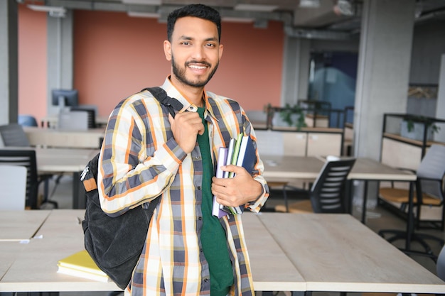 Young indian student boy reading book studying in college library with bookshelf behind working on assignment or project