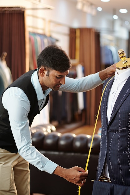 Young Indian tailor measuring front of suit jacket with tape