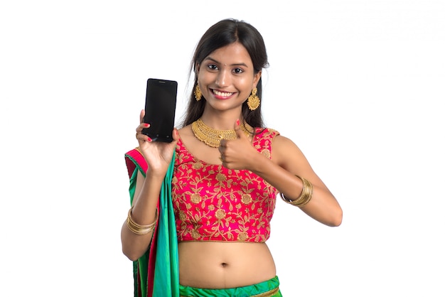 Young Indian traditional girl using a mobile phone or smartphone and showing blank screen smart phone on white background