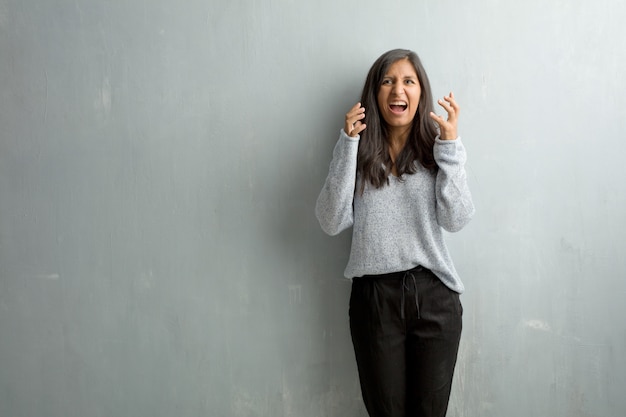 Young indian woman against a grunge wall very angry and upset, very tense, screaming furious