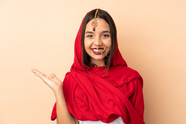 Photo young indian woman on beige wall holding blank space on the palm