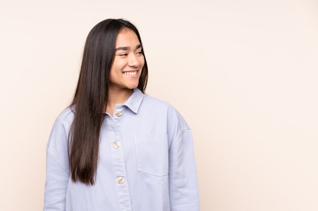 Young Indian woman on beige wall looking to the side and smiling