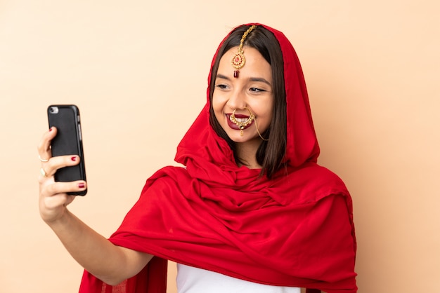 Selfieを作るベージュの壁に若いインド人女性