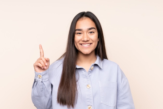 Young Indian woman on beige wall pointing up a great idea