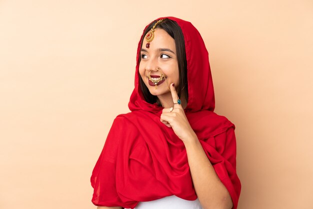 Young Indian woman on beige wall thinking an idea while looking up