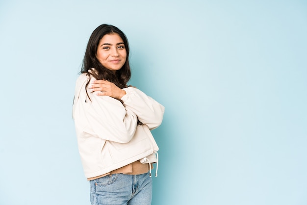 Young indian woman on blue hugs, smiling carefree and happy.