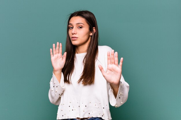 Young Indian woman on blue rejecting someone showing a gesture of disgust.